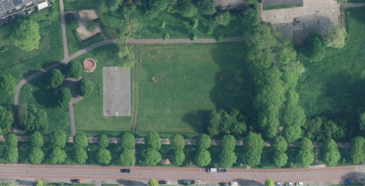 Luchtfoto van de huidige plek met veel gras, een basketbalveld en veel bomen.