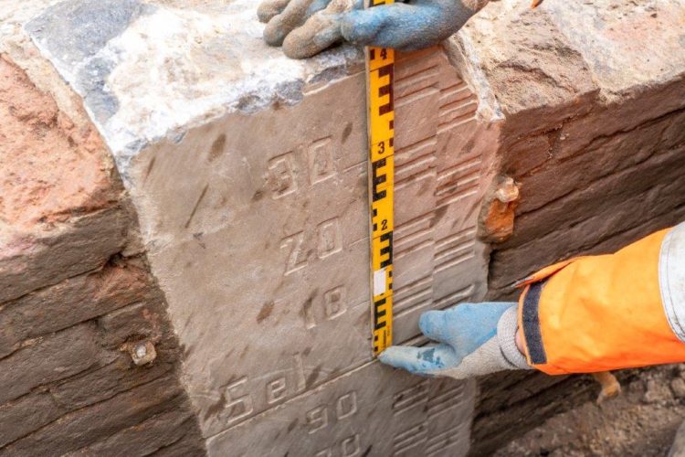 Archeoloog houdt een meetlint naast de ingemetselde natuurstenen peilschaal waarop men de waterstanden van de IJssel kon aflezen